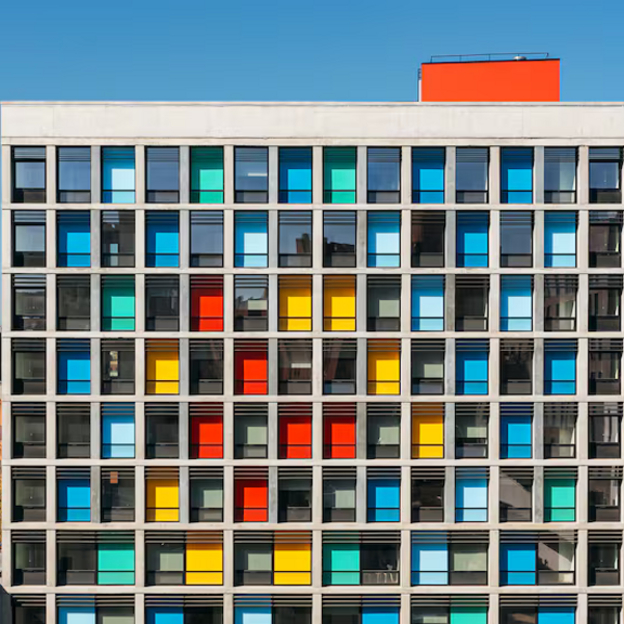 View of a large rectangular multifamily building with colored glass windows.