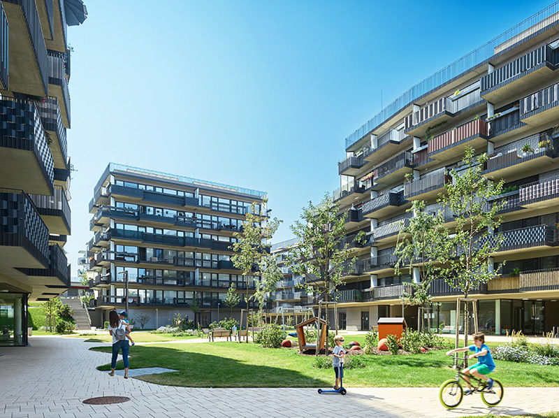 Seven-story residential buildings surround a lawn and playground. Balconies run the full length of the apartments, which have floor-to-ceiling windows.