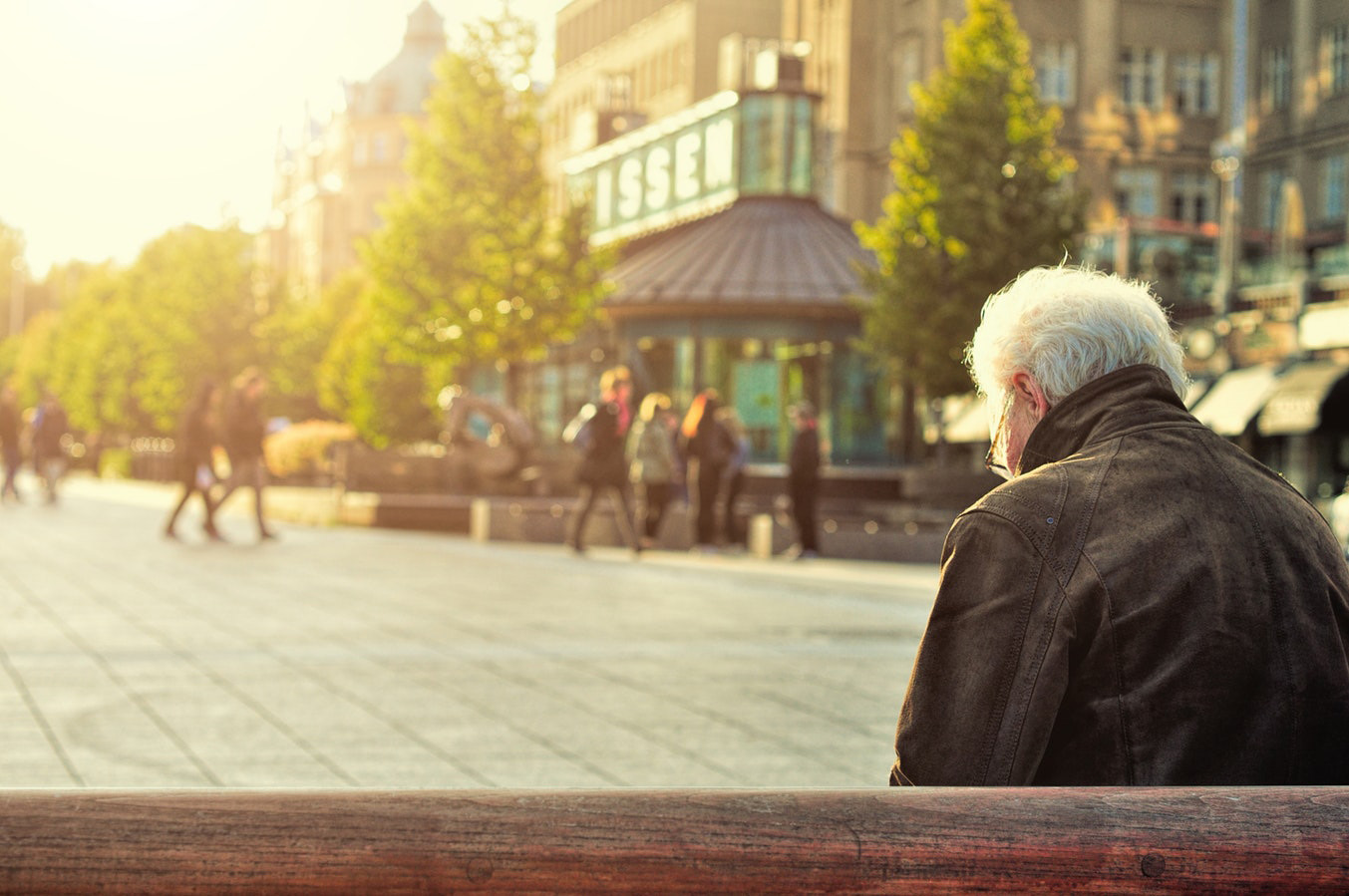 Older man sitting on bench in a public square.