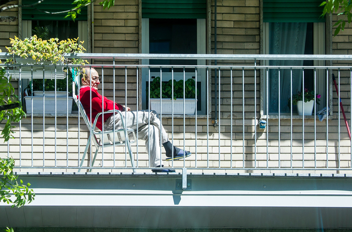 Older adult sitting on apartment balcony and looking out at neighborhood.