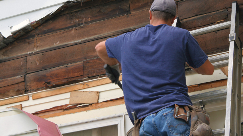 Man on a ladder removing old siding from a home.