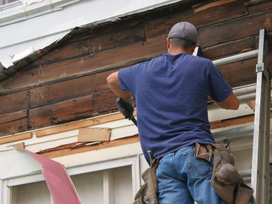 Man on a ladder removing old siding from a home.