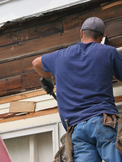 Man on a ladder removing old siding from a home.