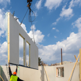 Crane placing a prebuilt wall into a home under construction.
