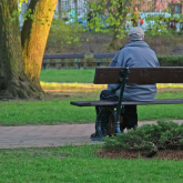 Older adult man sitting on a bench in a park.
