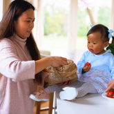 Mother giving strawberries to young child seated on kitchen countertop.
