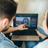 Couple pointing at real estate on laptop screen.