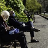 Two older adults sitting on a park bench near sidewalk.