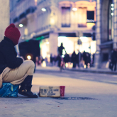 Woman experiencing homelessness sits by the sidewalk.