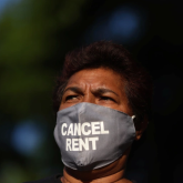 Person of color wearing a "cancel rent" face mask.