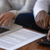 Man and woman calculating information using laptop and calculator.