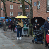 New Yorkers line up in the rain with carts and umbrellas.