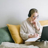 Young woman working on computer on bed.