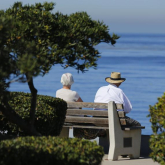Two older adults sitting by the ocean.