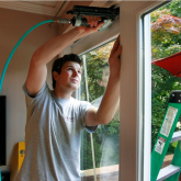 Man making home repairs to a wall with windows.