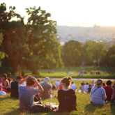 Group of young people sitting on hill overlooking city.