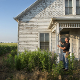 View of a man hammering a nail on the porch of an old house.
