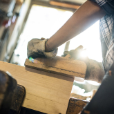 Woman shaping piece of wood in metal clamp.