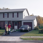 A family stands in the driveway outside their single-family house.