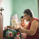 Older woman sewing at sewing machine with young boy watching.