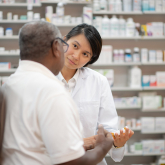 Older man talks to pharmacist while filling prescription.