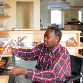 Older man in wheelchair cooking at a stovetop.