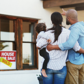 Couple with baby looking at house with "sold" sign.