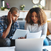 Couple considering bills in living room.
