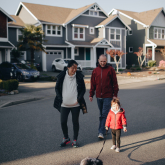 Family walking dog on suburban street.