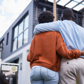Couple standing together staring up at house.