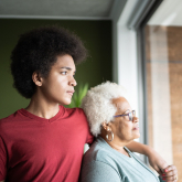 Younger man and older woman standing by window at home.