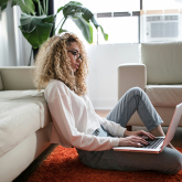 Young woman sitting on floor by couch with laptop.