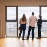 Three people staring out the window of an empty apartment