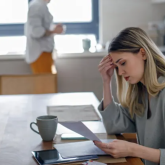 Worried woman sitting at dining table looking at documents with hand on head