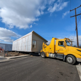 View of a large truck with part of a prefabricated home on the bed.
