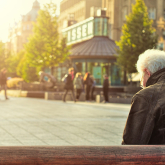 Older man sitting on bench in a public square.