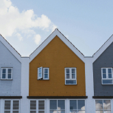 Facades of three townhouses with pitched roofs.