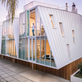 An exterior view of Lorcan O'Herlihy Architects' Canyon Drive development shows a series of four townhouses with inflected roofs and glass facades, all sitting atop private single-car garages clad in wood.