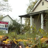 House with an overgrown front yard and for sale sign.