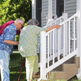 Two older adults climbing stairs to a home.