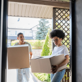 Couple carrying boxes into a house.