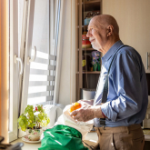 Older adult man looking out kitchen window.