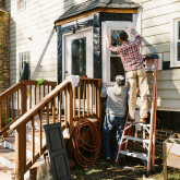 Two people outside a house fixing a window