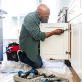 Man installing door on kitchen cabinet.