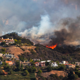 Homes on a hill with wildfire in the background.