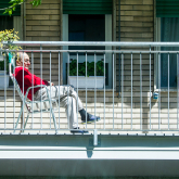Older adult sitting on apartment balcony and looking out at neighborhood.