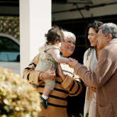 Older Hispanic couple greeting daughter and grandchild outside their home.