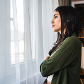 Young woman looking out apartment window.