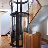 A pneumatic elevator next to a staircase in a multilevel home.