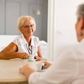 Two older adult woman sitting at kitchen table.